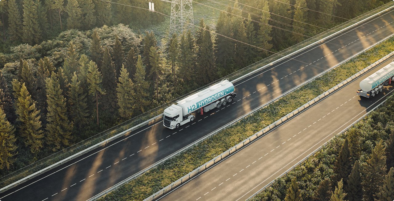 A drone shot shows a tanker truck driving on a multi-lane highway through a dense forest, with other vehicles in the distance.