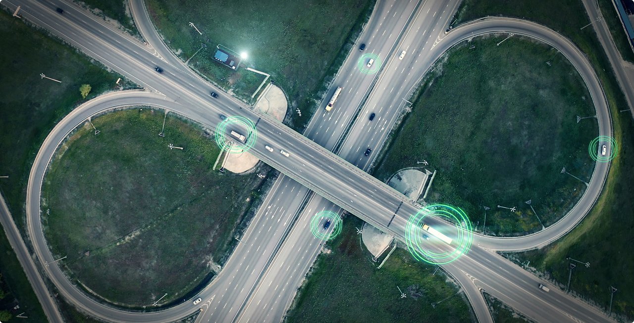 Aerial view of a complex highway interchange or junction, winding over green areas, with glowing dots that could represent traffic flows or sensor data.