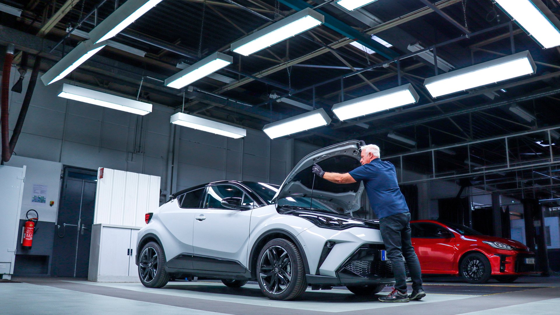 A technician inspects a white car under the hood in a modern workshop – vehicle inspection and engineering.