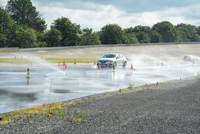 Car on a wet test track during a driving maneuver with water fountains – driver safety training or vehicle testing.
