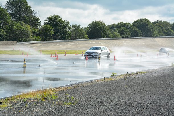 Car on a wet test track during a driving maneuver with water fountains – driver safety training or vehicle testing.