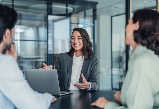 Businesswoman talking with two colleagues in a modern meeting room, appearing friendly and engaged.