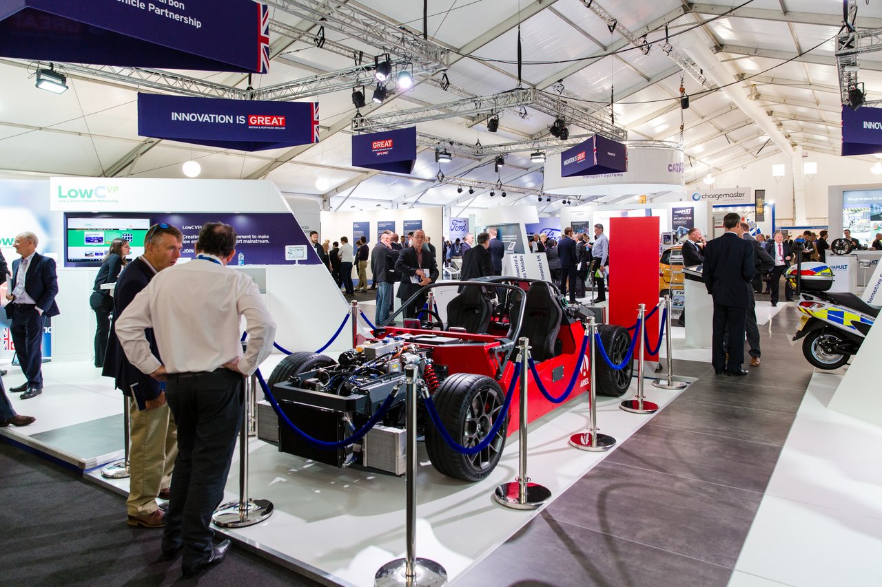 Automotive trade fair with visitors and exhibits in a modern exhibition hall.