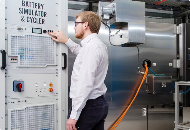 Ein junger Mann mit Brille in einem weißen Hemd bedient ein Bedienfeld an einer industriellen Maschine oder einem Schaltschrank.