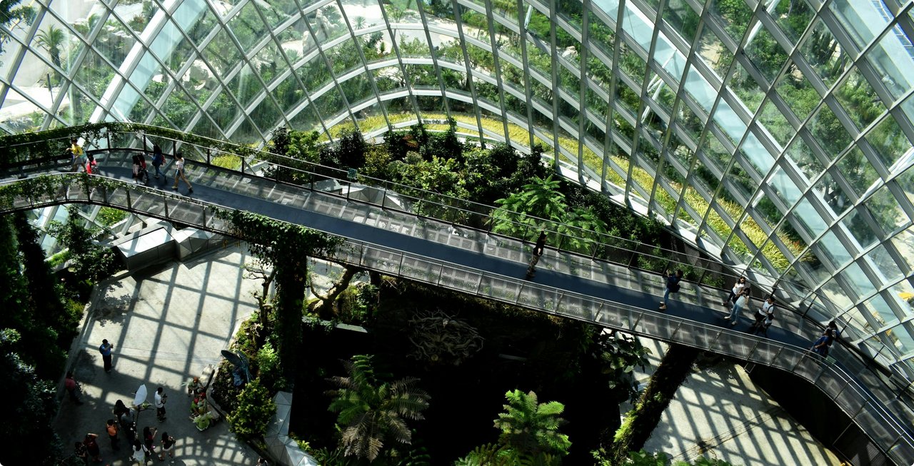 An interior view of a modern building with a glass facade and multiple levels of lush green plants, creating a vertical garden or atrium environment.