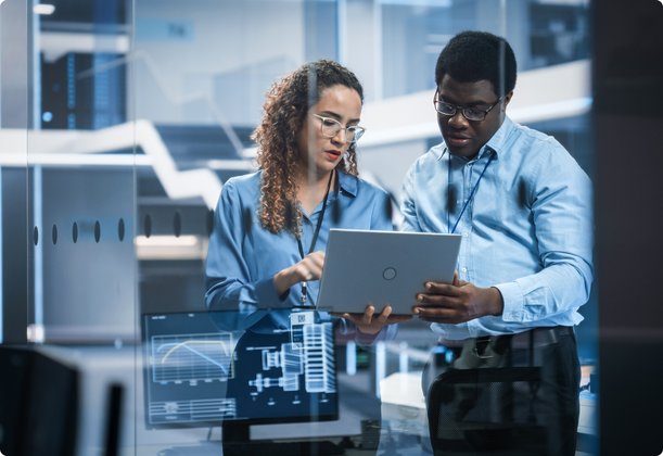 Two professionals, a woman and a man, stand in a modern office or server room, jointly looking at a laptop, representing collaboration and technology utilization. Holographic elements are visible in the foreground.