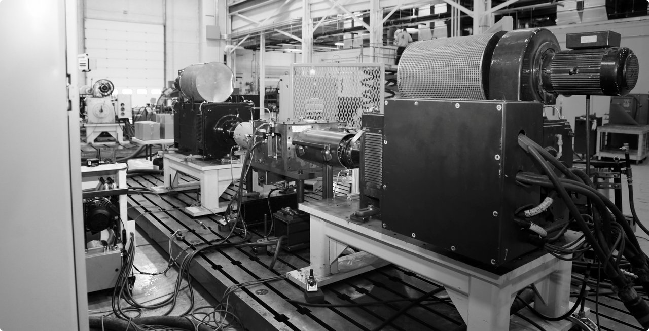 Une image en noir et blanc d'un laboratoire ou d'une installation de recherche avec des machines complexes et des dispositifs optiques montés sur des bancs. De nombreux câbles, lentilles et composants métalliques sont visibles, suggérant des mesures de précision ou des expériences.