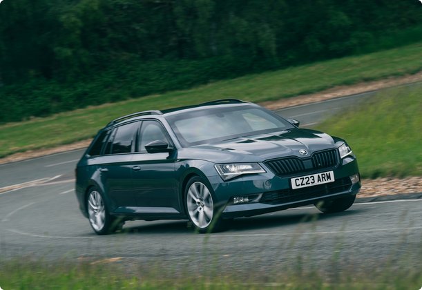 A dark grey or dark blue station wagon drives on a winding road through a green landscape.
