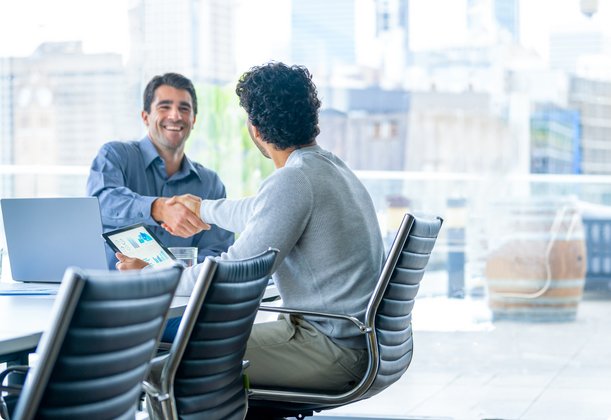 Two businessmen shaking hands in a modern conference room with a city view.