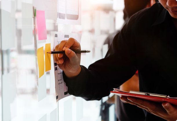 Person writing notes on sticky notes on a whiteboard with a pen, holding a tablet in the other hand.