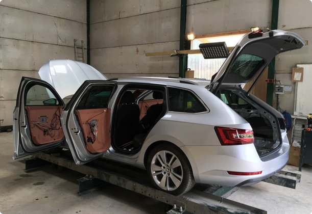 A silver station wagon stands in a workshop with all doors, the hood, and the trunk lid open, likely for repair or modification.