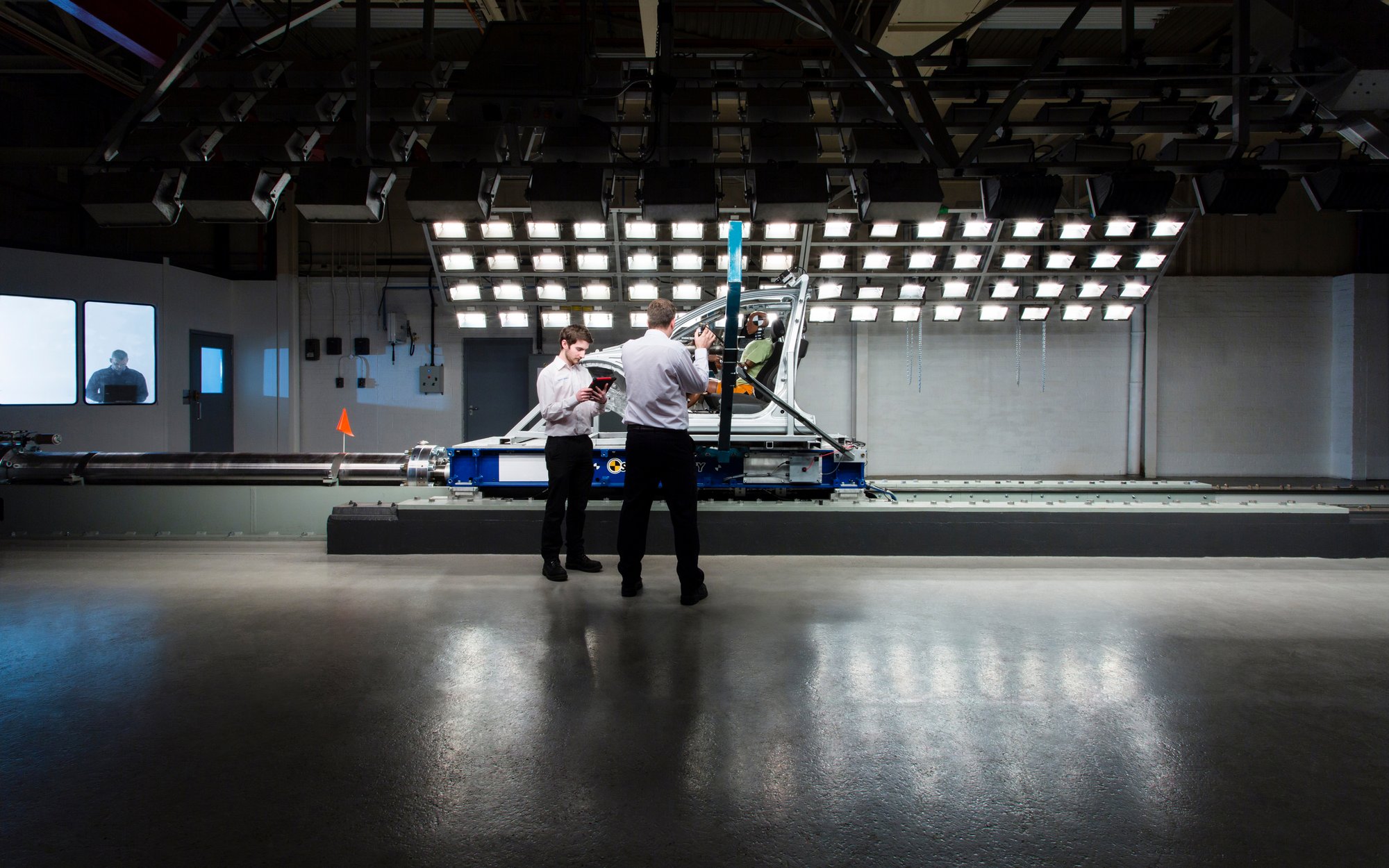 Two people stand in front of a large testing setup featuring numerous lights and cameras, possibly in a laboratory for lighting or imaging tests.