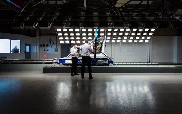 Two people stand in front of a large testing setup featuring numerous lights and cameras, possibly in a laboratory for lighting or imaging tests.