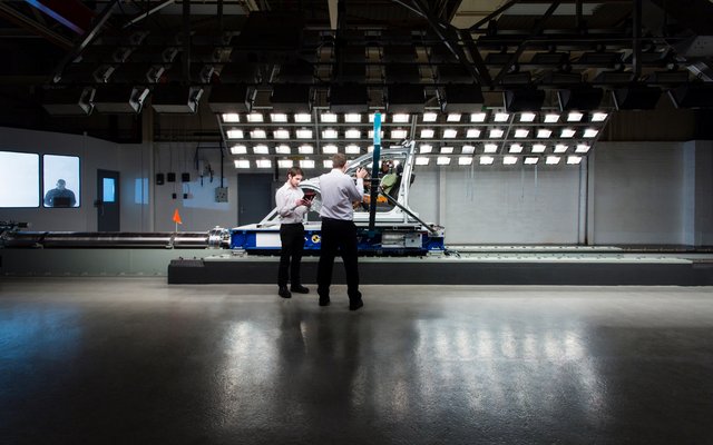 Two people stand in front of a large testing setup featuring numerous lights and cameras, possibly in a laboratory for lighting or imaging tests.