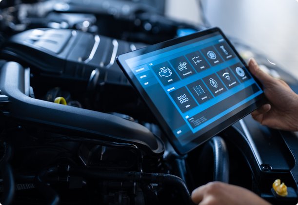 A close-up shot shows a person holding a tablet with diagnostic software or performance data in front of an open car engine, indicating modern vehicle maintenance or analysis.