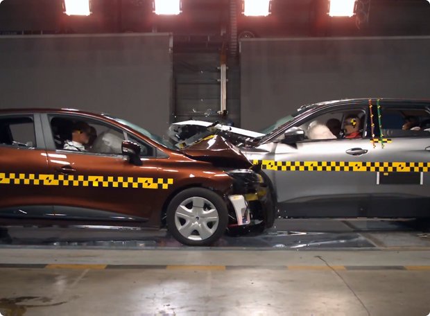 Two cars, one brown and one grey, colliding head-on in a crash test. The fronts of both vehicles are heavily deformed, and the airbags are visibly deployed. Both vehicles feature black and yellow markings.
