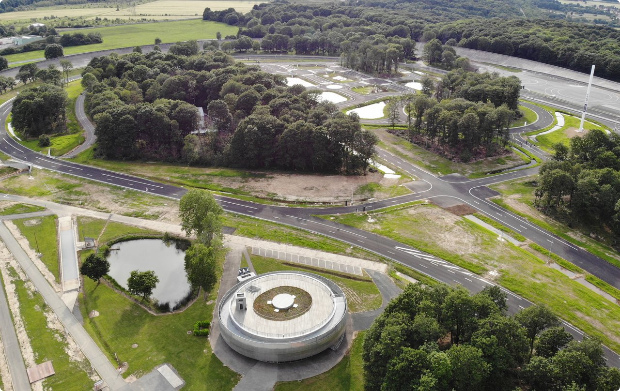 Aerial view of an expansive proving ground with a circular building, asphalt roads, and lush green vegetation.