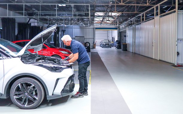 Technician working on a white vehicle in a modern testing facility – open hood visible.