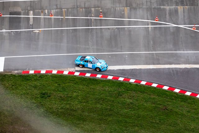 A blue and white race car drives on an asphalt track, next to a grassy area with red and white curbing.