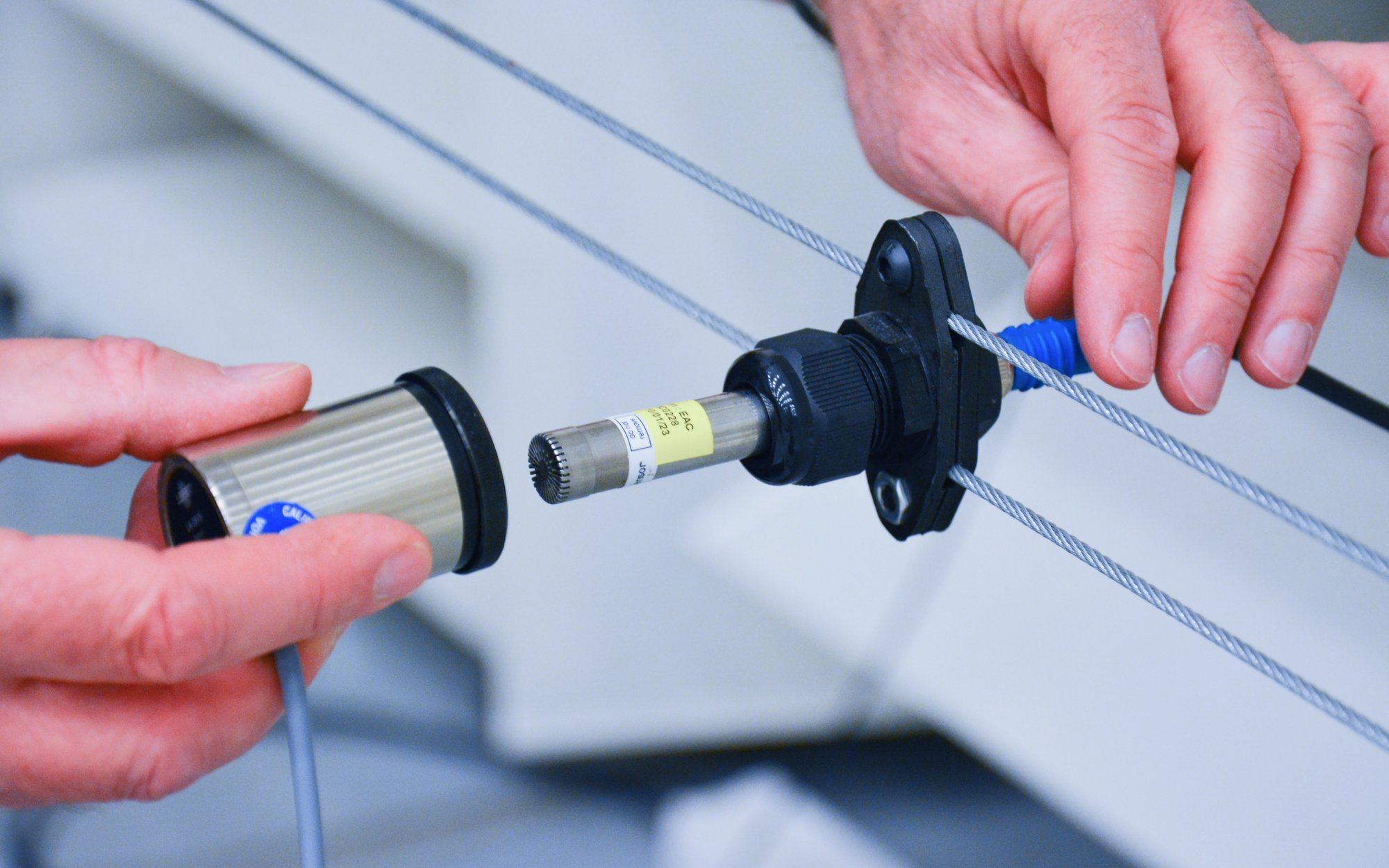 Close-up of hands connecting a technical device with cables, possibly a sensor or connector.