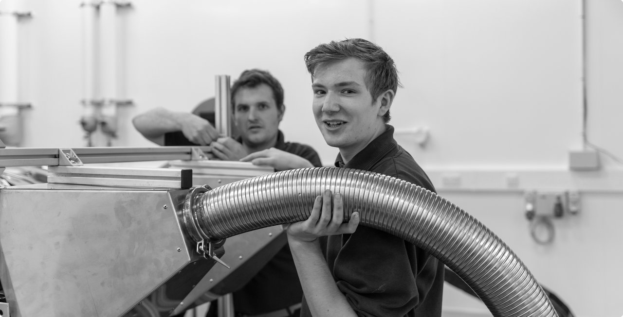 Two young men working together on a large metal component in a workshop – teamwork in a technical setting.