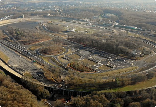 Une vue aérienne présente une grande piste d'essai située dans une zone boisée avec plusieurs voies et des bâtiments à l'intérieur de l'ovale. Les arbres sont dénudés, ce qui suggère l'automne ou l'hiver.