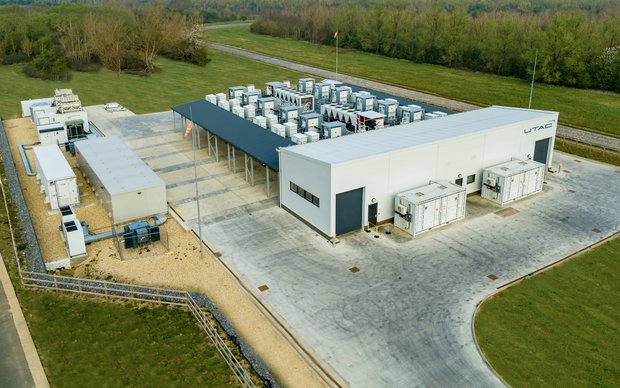 An aerial view of a large industrial facility with several buildings and open areas, surrounded by trees and a rural landscape.