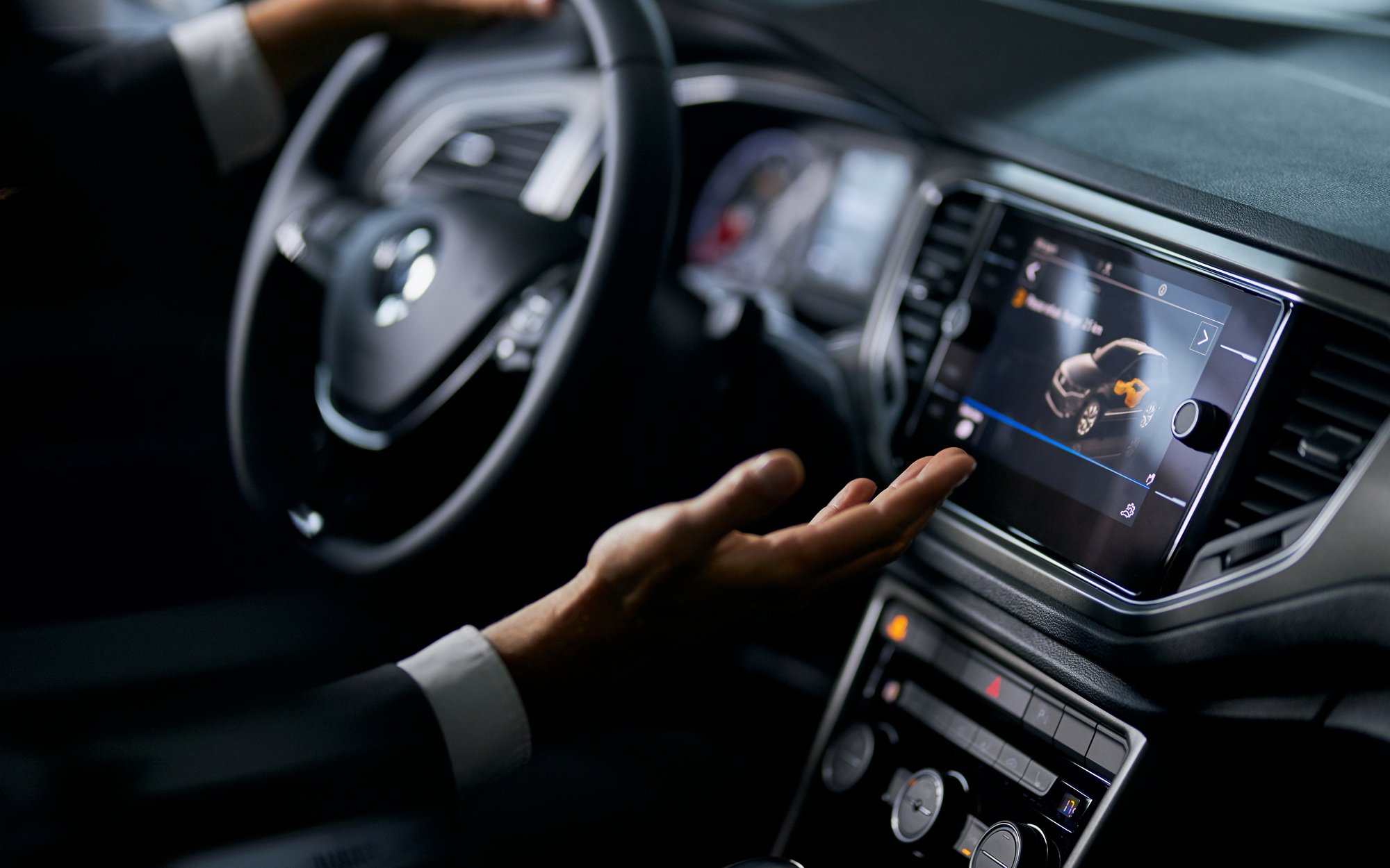 Close-up of a person's hands interacting with the touchscreen and steering wheel of a modern car's infotainment system.