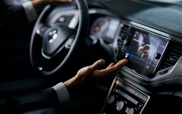 Close-up of a person's hands interacting with the touchscreen and steering wheel of a modern car's infotainment system.