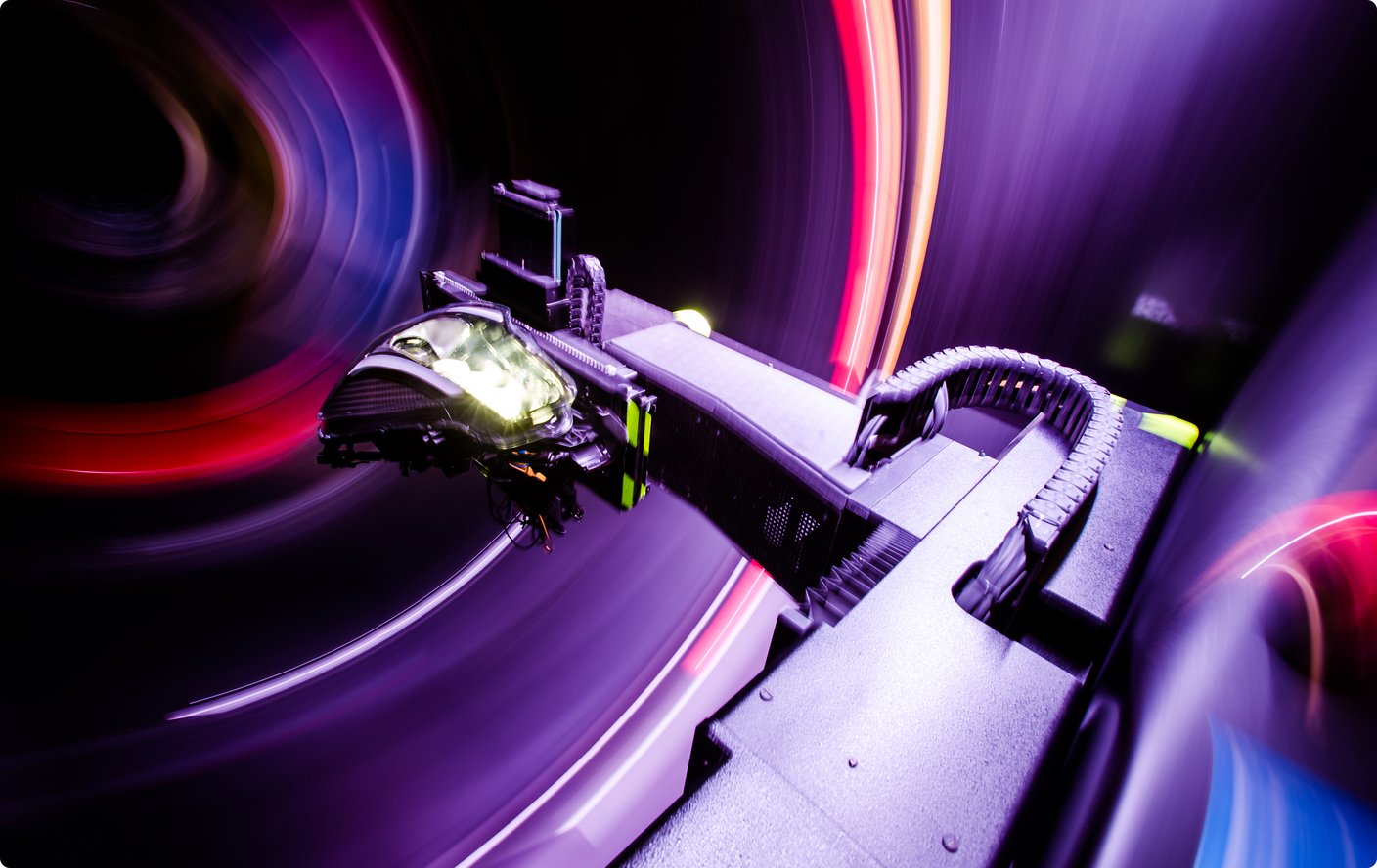 Un gros plan d'une partie d'une machine ou d'un appareil avec des traînées de lumière floues, violettes et rouges lumineuses en arrière-plan, suggérant le mouvement.