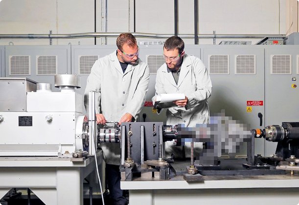 Two men in white lab coats work together on precision machinery in a clean laboratory or workshop.