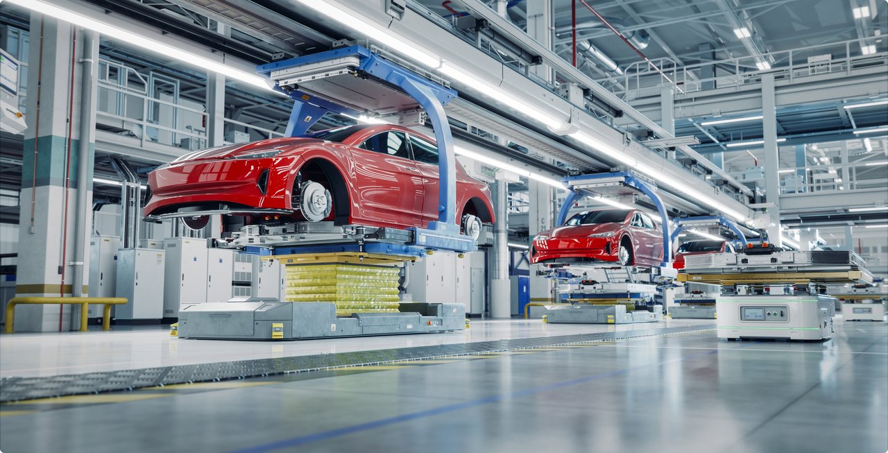 A modern automotive production line in a brightly lit factory hall, where red car bodies are transported overhead by automated systems and placed onto automated guided vehicles (AGVs). The scene depicts the vehicle assembly process with high precision and automation.
