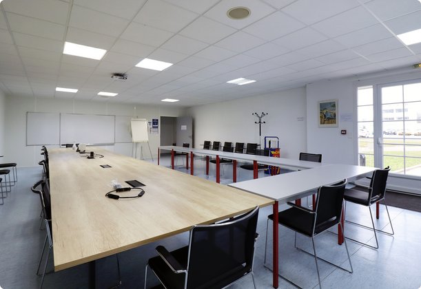 A spacious, bright training or meeting room with a large U-shaped table configuration and individual tables, equipped with computers and chairs.
