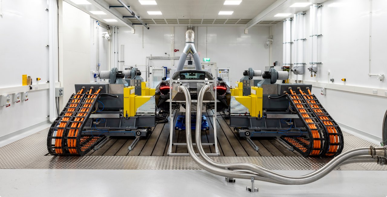 A large, complex industrial machine or test rig with two prominent track-like conveyor belts on either side, used for material handling or processing, is shown in a clean, brightly lit workshop or laboratory environment.