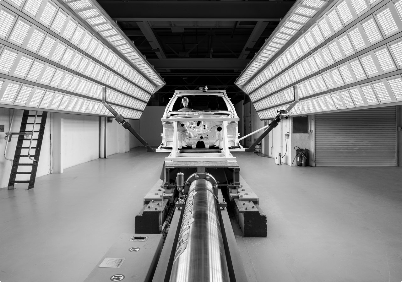 Une carrosserie de voiture vide sur un banc d'essai dans une salle d'essai fortement éclairée avec des rangées de lumières sur les côtés.