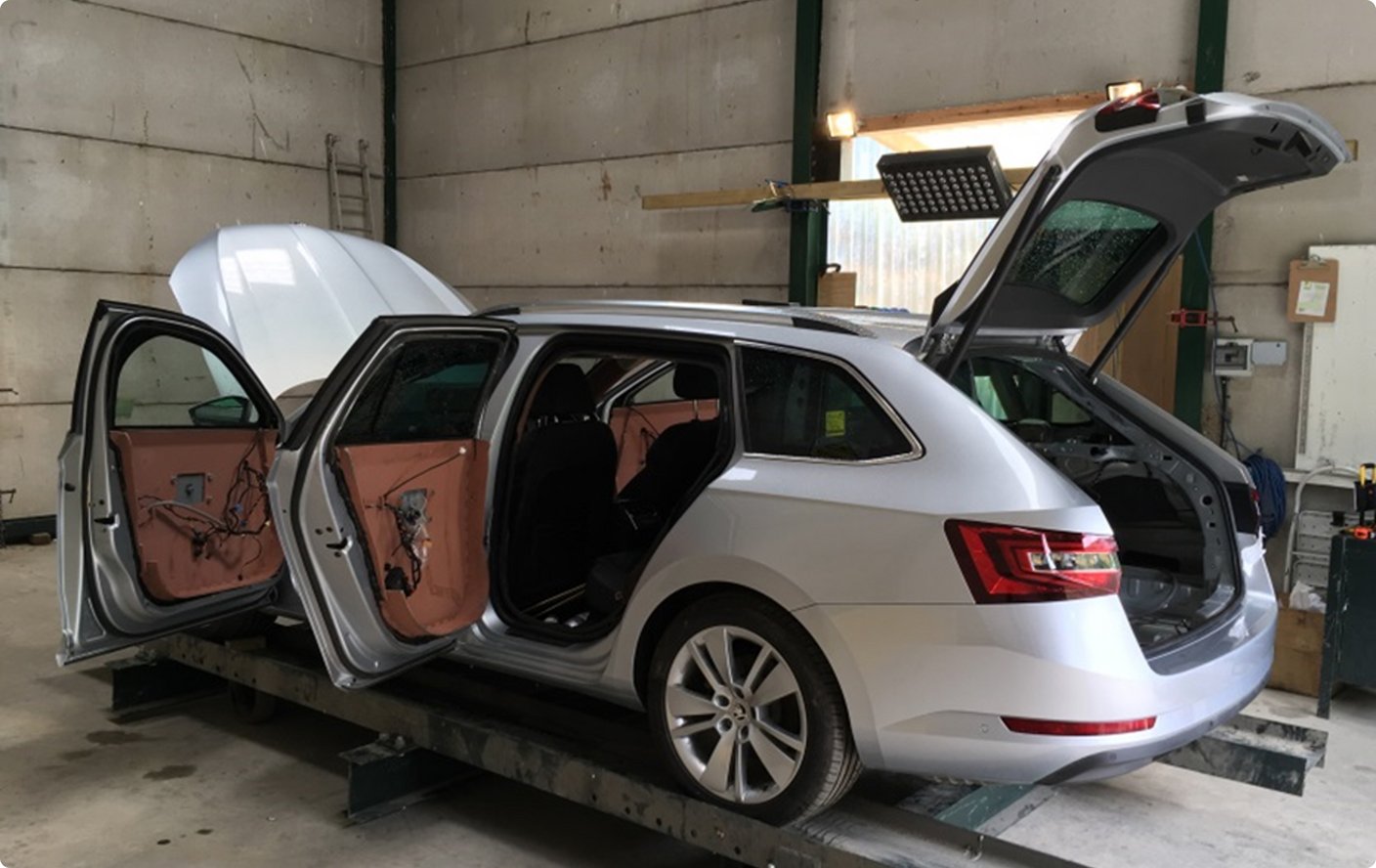 Ein hellfarbener Kombi steht in einer Werkstatt oder Garage mit allen Türen und der Heckklappe geöffnet, was auf Reparatur, Anpassung oder Vorbereitung hindeutet.
